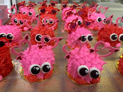 Colorful cupcakes shaped like cute creatures, decorated with pink frosting, big eyes, and heart-shaped toppers.