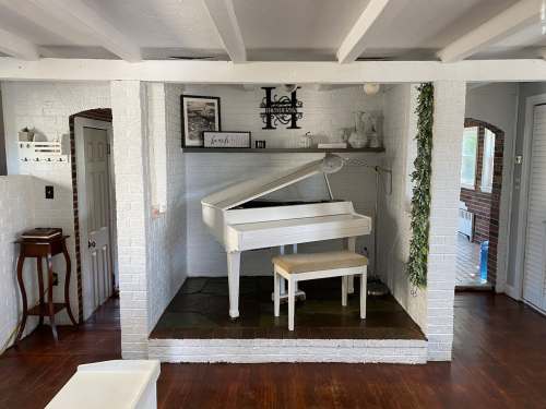 A bright room featuring a white grand piano on a stone platform, with decorative shelves and wooden flooring.