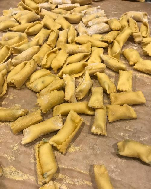 A close-up of freshly made pasta, shaped and dusted with flour, scattered on a wooden surface.