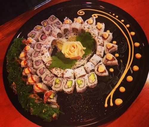 A beautifully arranged platter of sushi rolls, featuring various types and garnished with a rose and decorative sauces.
