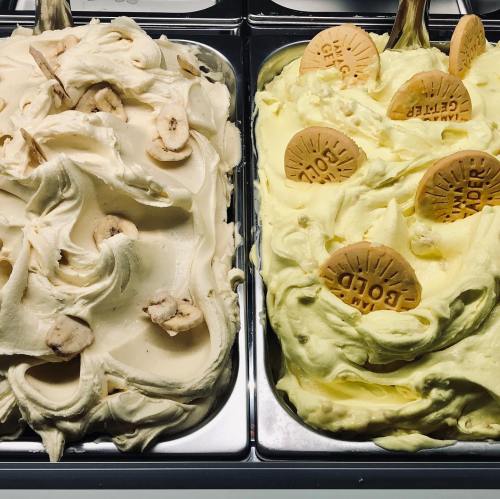 Two tubs of gelato: one with banana slices and the other lemon-flavored, both topped with round cookies.