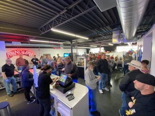 A busy indoor venue with a crowd of people waiting in line, some at a counter, and colorful decorations in the background.