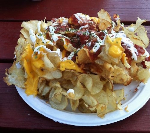 A plate of loaded potato chips topped with cheese, sour cream, and herbs.