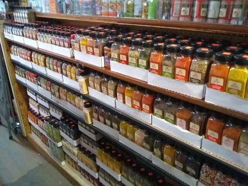 A neatly organized shelf filled with various jars of spices and herbs in a store.