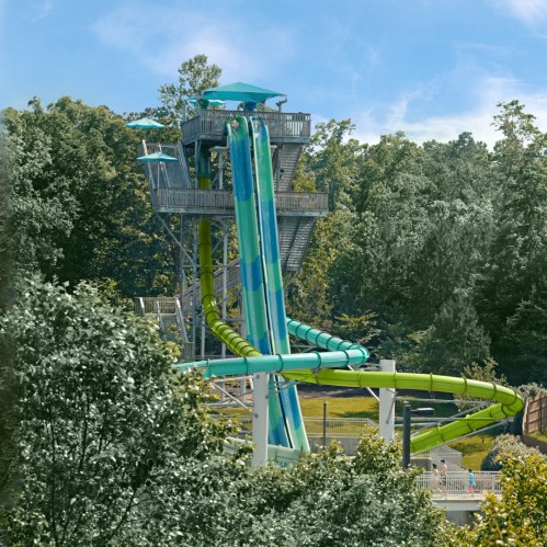 A tall water slide with a blue and green design, surrounded by trees and a grassy area.