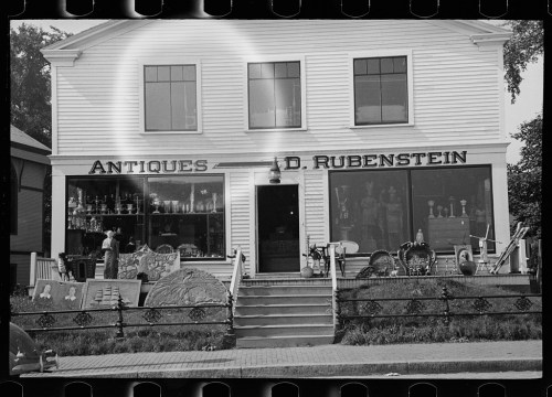 A vintage shop front displaying antiques, with large windows and a sign reading "A.D. Rubenstein."