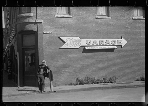 A man stands by a building with a sign reading "Fireproof Garage" and an arrow pointing towards the entrance.