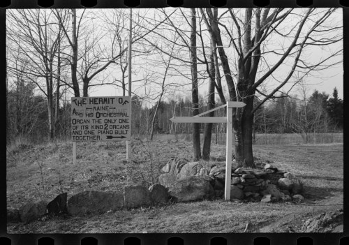 Signpost for "The Hermit" with a message about a unique musical creation, surrounded by trees and rocks.