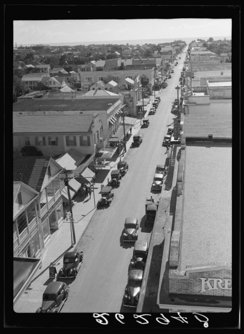 Aerial view of a historic street lined with vintage cars and buildings, showcasing a bustling town scene.