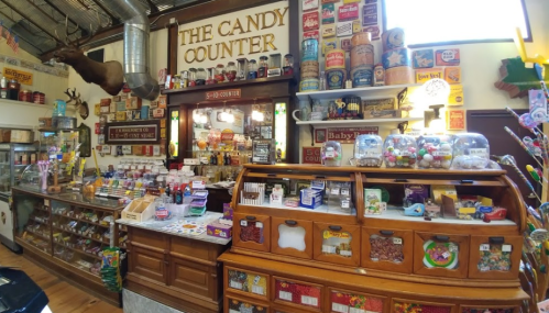 A vintage candy shop filled with colorful jars, sweets, and nostalgic decor, featuring a wooden counter and shelves.