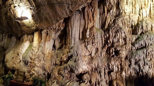 Stalactite and stalagmite formations on a cave wall, illuminated by a ceiling light.