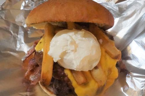 A hearty burger topped with cheese, fries, bacon, and a dollop of sour cream, served in a toasted bun.