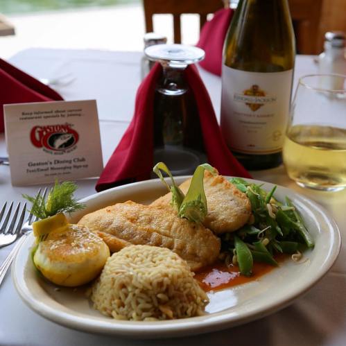 A plate of fish with rice, salad, and lemon, set on a table with a wine bottle and napkins.