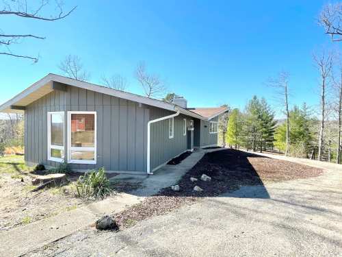 A modern gray house with a sloped roof, surrounded by trees and a clear blue sky.