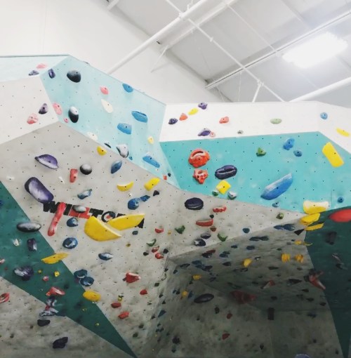 Indoor climbing wall with colorful holds on a textured surface, featuring various routes and angles.