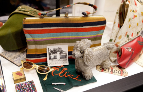 A colorful striped handbag, vintage sunglasses, a beaded dog figurine, and a photo on a display table.