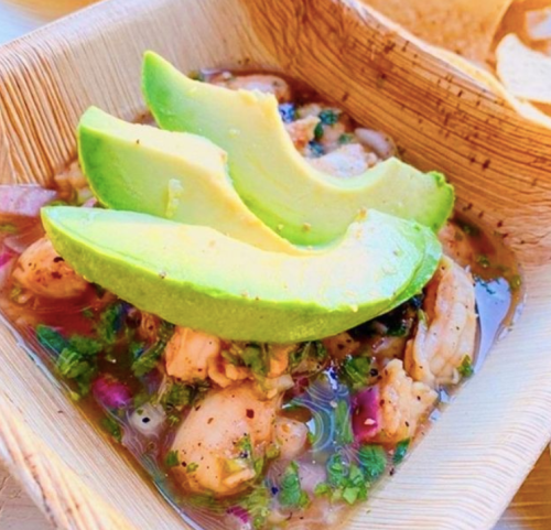 A wooden bowl filled with ceviche topped with avocado slices and garnished with herbs and onions.