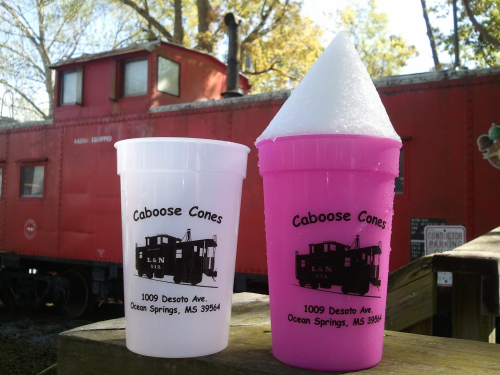 Two colorful cups with "Caboose Cones" branding in front of a red train caboose. One cup is pink, the other is white.