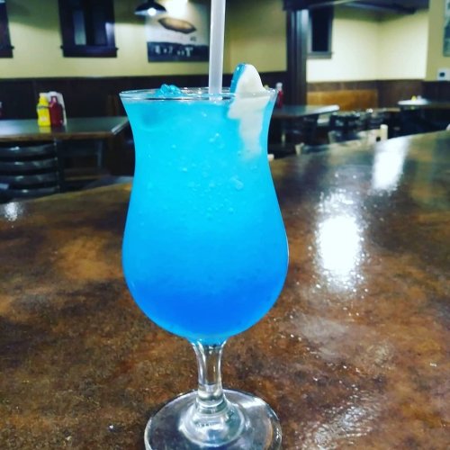 A vibrant blue cocktail in a tall glass with ice, sitting on a polished wooden bar.
