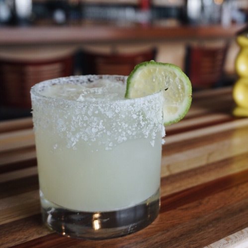 A refreshing margarita in a glass with a salted rim and a lime wedge, set on a wooden bar top.