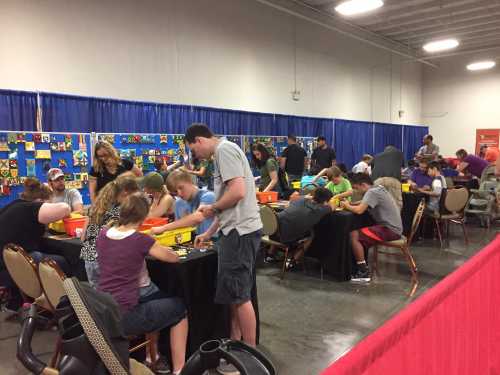 A busy event space with people gathered around tables, working on colorful projects and engaging in activities.