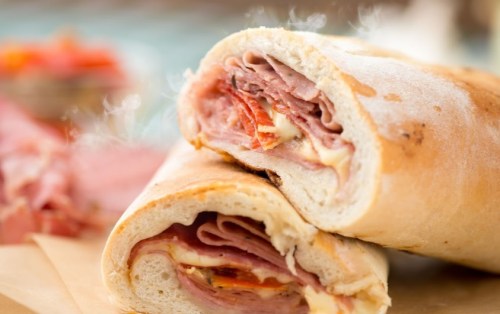 A close-up of a sliced sandwich filled with layers of meats and cheese, with steam rising from the fresh bread.