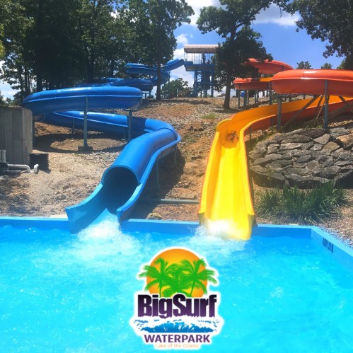 Colorful water slides at Big Surf Waterpark, with a blue pool in the foreground and trees in the background.