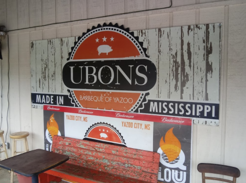Sign for Ubon's Barbeque in Yazoo City, Mississippi, featuring a rustic design and a red bench in front.