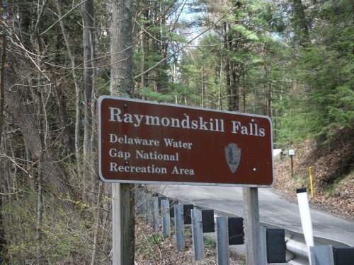 Sign for Raymondskill Falls in Delaware Water Gap National Recreation Area, surrounded by trees and a road.