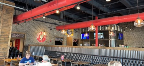 Interior of a restaurant featuring brick walls, red ductwork, pendant lights, and a bar area with seating.