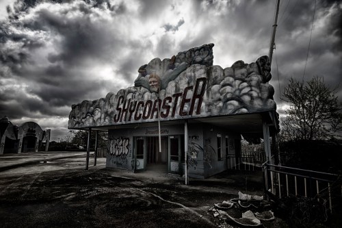 Abandoned building with "Skycoaster" sign, graffiti, and dark, cloudy sky overhead.