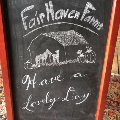 Chalkboard sign for Fair Haven Farms with a drawing of a barn, horses, and pumpkins, wishing a lovely day.