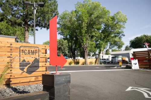 A red arrow sign points left at a campsite entrance, surrounded by trees and wooden structures.