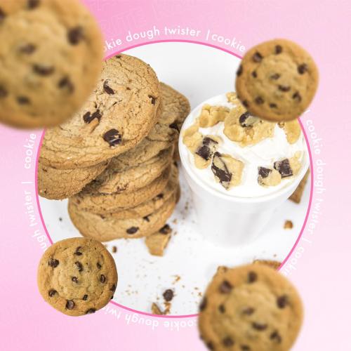 A stack of chocolate chip cookies beside a cup of cookie dough topped with cookie pieces, on a pink background.