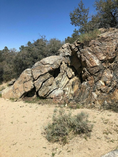 A large, textured rock formation surrounded by sparse vegetation under a clear blue sky.