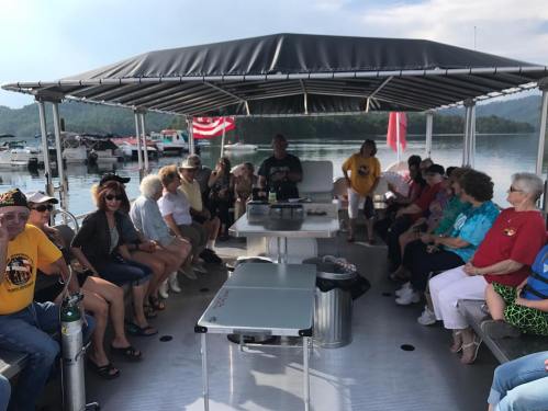 A group of people sitting on a boat under a canopy, enjoying a gathering by the water with scenic views.