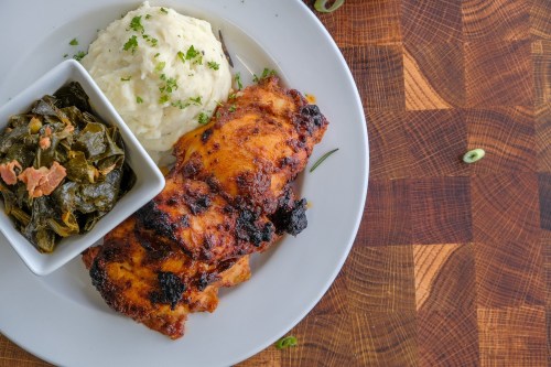 A plate featuring grilled chicken, creamy mashed potatoes, and a side of collard greens, garnished with herbs.