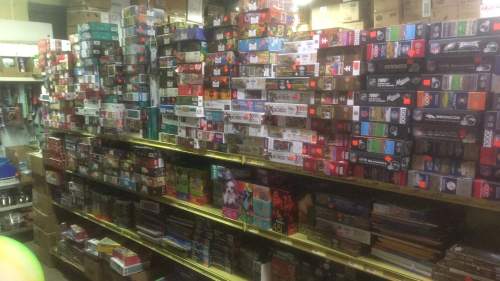 A cluttered room filled with shelves stacked high with various board games and puzzles, some with price tags.