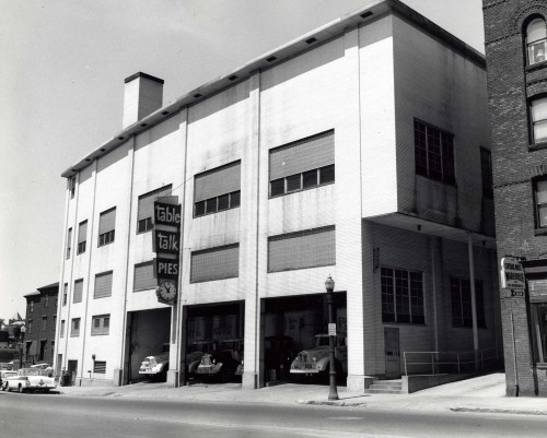 Black and white photo of a building with "Table Talk Pies" sign, featuring parked cars and a street view.