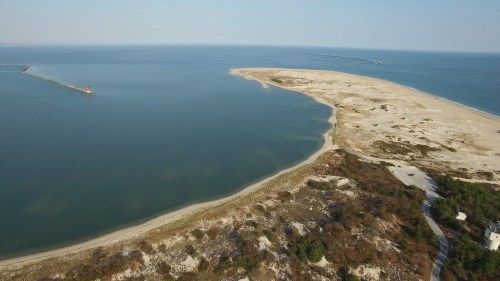 Aerial view of a sandy peninsula extending into calm blue waters, with a distant boat navigating the coastline.