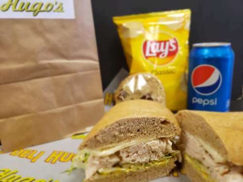 A sandwich with turkey and lettuce, a bag of Lay's chips, and a can of Pepsi, all on a table with a brown paper bag.