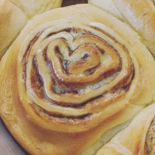 Close-up of a freshly baked cinnamon roll with a glossy, swirled topping and a golden-brown crust.