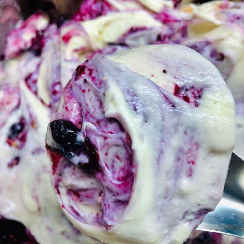A close-up of a scoop of creamy ice cream swirled with berry sauce, showcasing rich colors and textures.