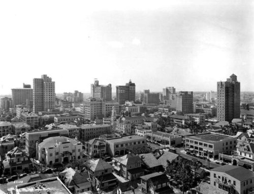 A black and white aerial view of a city skyline featuring tall buildings and a mix of architectural styles.