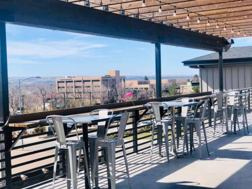 A rooftop patio with metal chairs and tables, overlooking a cityscape under a clear blue sky.