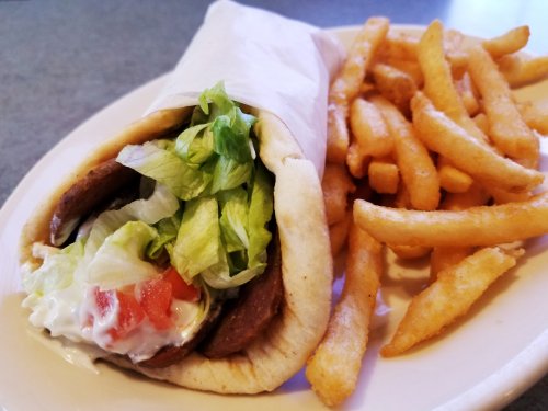 A pita wrap filled with lettuce, tomato, and meat, served with a side of golden French fries.