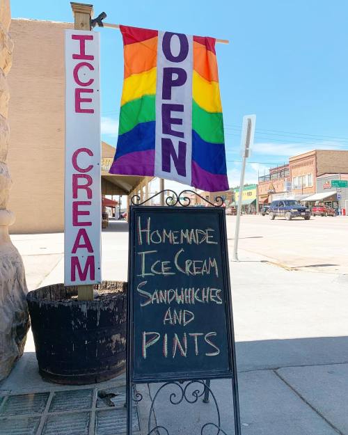 A sign outside an ice cream shop reads "Open" with a rainbow flag, advertising homemade ice cream, sandwiches, and pints.