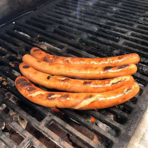 Four grilled sausages sizzling on a barbecue grill, with a smoky background.