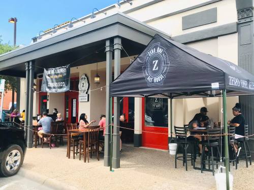 Outdoor seating area of a restaurant with a tent, tables, and people dining. Signs display the restaurant's name.