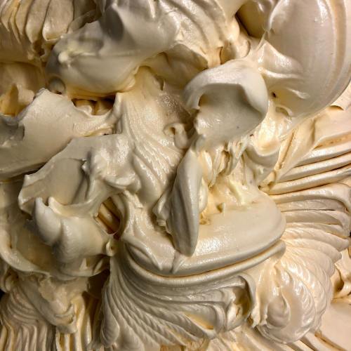 Close-up of creamy, swirled texture resembling whipped cream or soft serve ice cream in a light beige color.